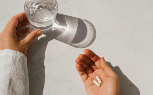 Nahrungsergänzungsmittel auf Handfläche neben einem Glas