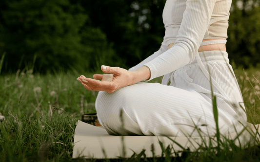Person sitzt entspannt in Schneidersitz auf Yogamatte in einer Wiese