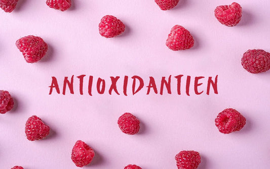 Das Wort "Antioxidantien" auf einem rosa Hintergrund, umgeben von einzelnen Himbeeren.