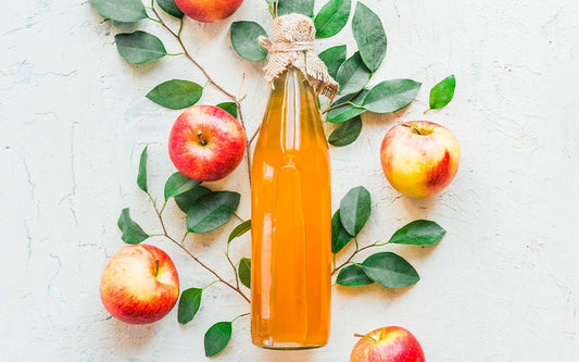 Flasche mit Apfelessig neben Äpfeln und grünen Blättern.