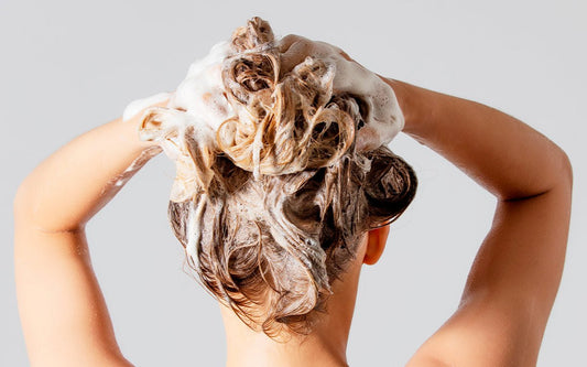 Frau shamponiert sich die Haare ein.