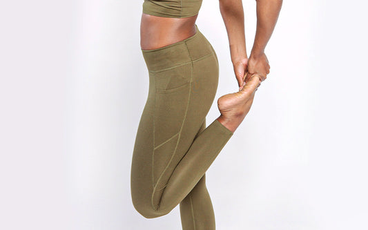 Frau in olive-grüner Sport Leggings dehnt ihr linkes Bein. 