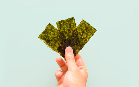 Hand hält drei Nori-Algen-Blätter nach vorne.