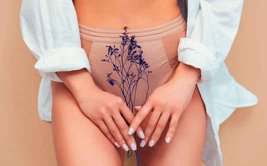 Frau steht in Bluse und Panty und hält mit beiden Hände Blumen vor ihren Beinen.