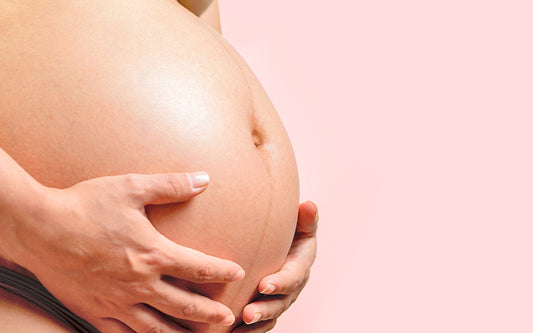 Frau hält schwangeren Bauch auf rosa Hintergrund