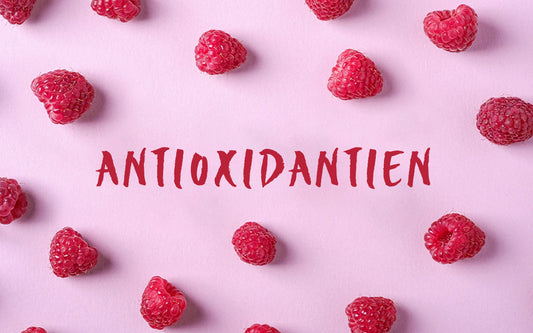Das Wort "Antioxidantien" auf einem rosa Hintergrund, umgeben von einzelnen Himbeeren. 