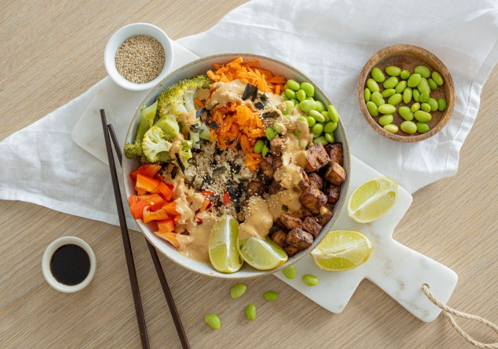Poke Bowl mit Miso-Tofu, Brokkoli, Edamame und Algen-Topping. Dekoriert ist das Ganze mit Edamame, Limetten, Sesam, Spießen und Soßa-Sauce