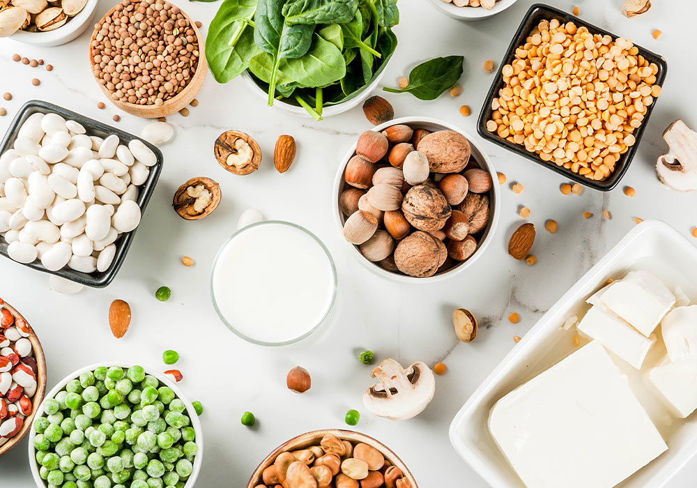 Verschieden Nüsse, Erbsen, Bohnen und Tofu in Schälchen auf einem marmorierten Tisch
