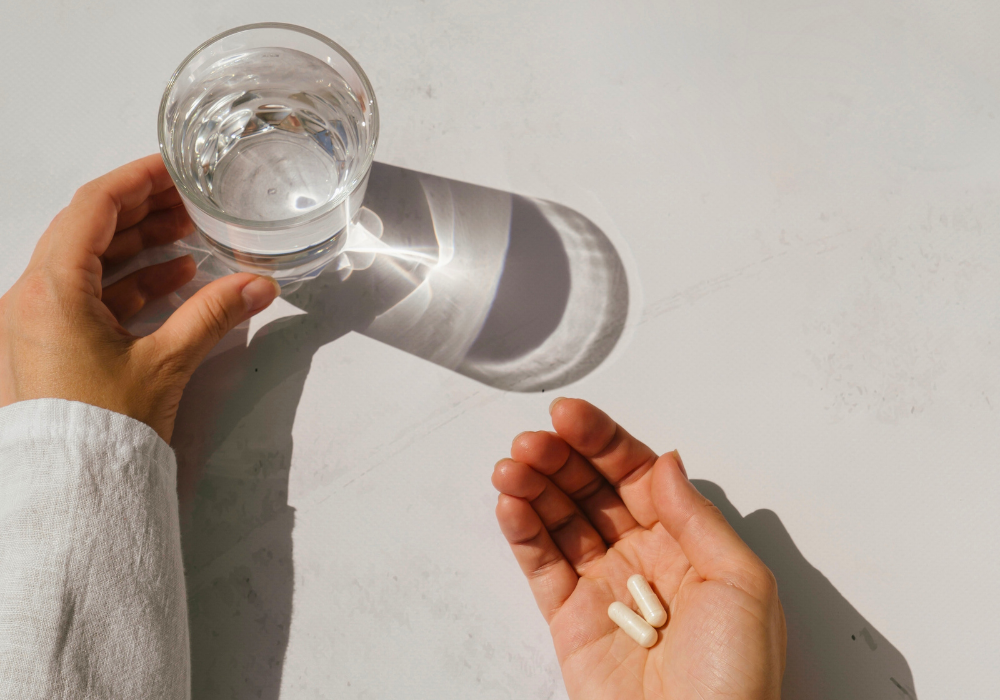 Nahrungsergänzungsmittel auf Handfläche neben einem Glas Wasser