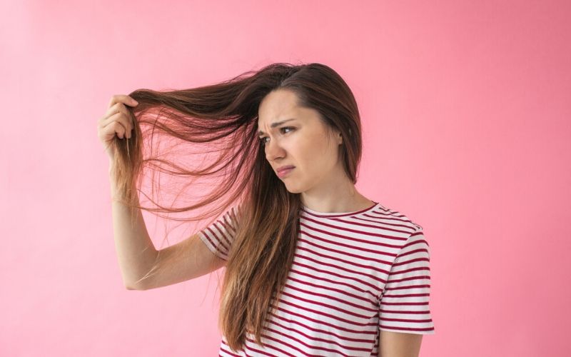 Unglückliche Frau im gestreiften T-Shirt mit Haarausfall vor einer pinken Wand