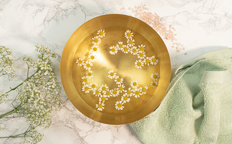 Goldene Schüssel mit Wasser und Kamillenblüten auf marmoriertem Hintergrund