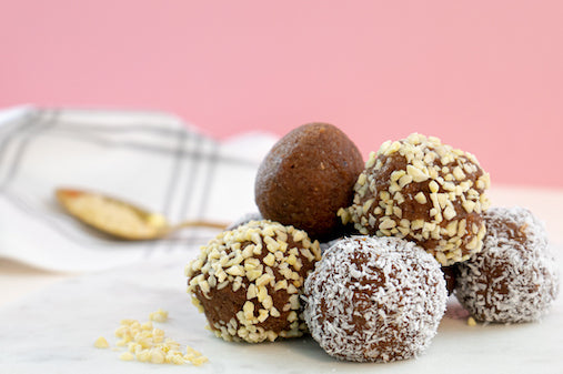 Blissballs mit verschiedenen Toppings vor rosa Hintergrund