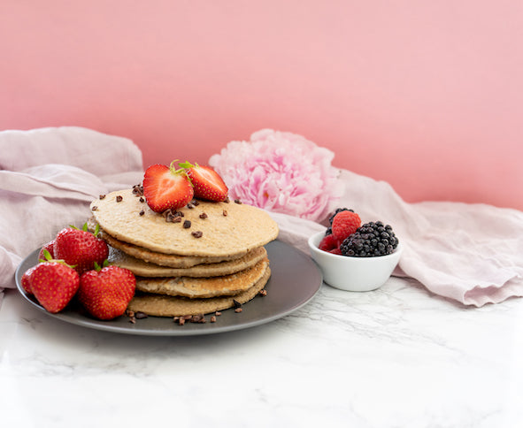 Pancakes auf grauem Teller mit Erdbeeren vor rosa Hintergrund