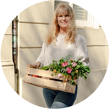 blonde-frau-haelt-obstkiste-mit-blumen-und-einkaeufen-in-derhand-lacht